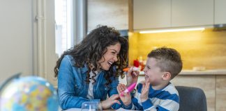 Mother helping with homework to her son indoor. Family, children and happy people concept. Mother and sons drawing together, mom helping with homework