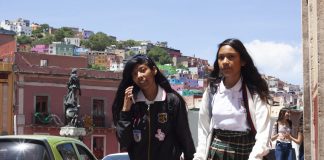 girl walking in school uniform with a friend who talks to the mobile with the town of colorful houses behind. Guanajuato, Mexico,